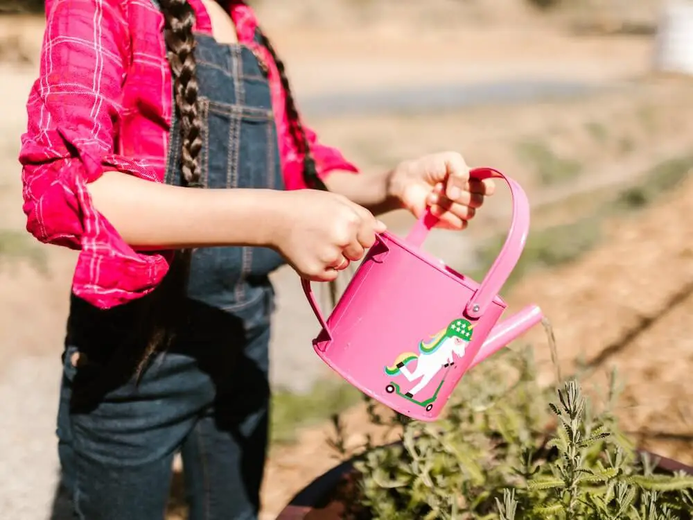 Girl watering plants in a container with a mini pink watering can with a unicorn.